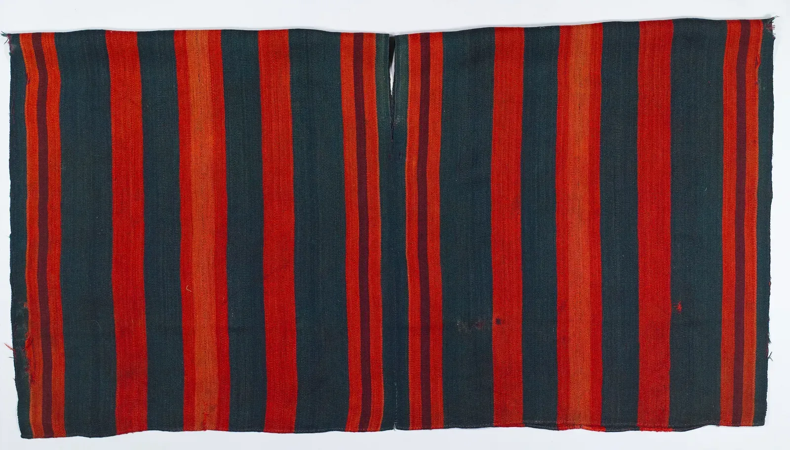 Woven wool poncho laid flat, with vertical red and dark blue-green stripes, made of two panels joined at the centre with a neck opening